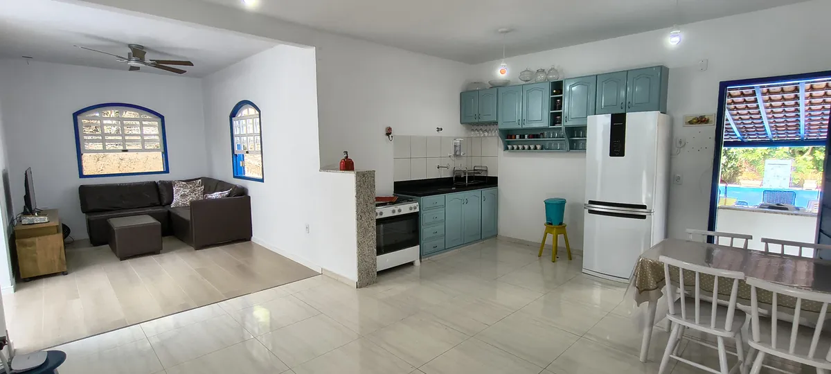Ambiente integrado com sofá, cozinha colonial azul, mesa de jantar e ventilador de teto no Sítio Canto da Seriema