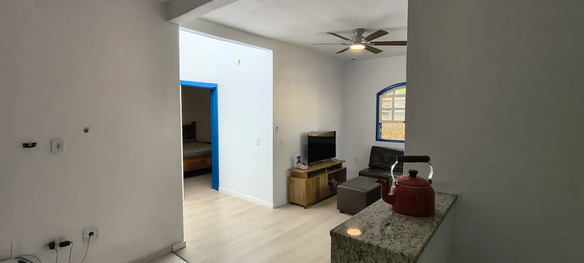 Vista da sala de estar com bancada em granito, TV e acesso aos quartos no Sítio Canto da Seriema
