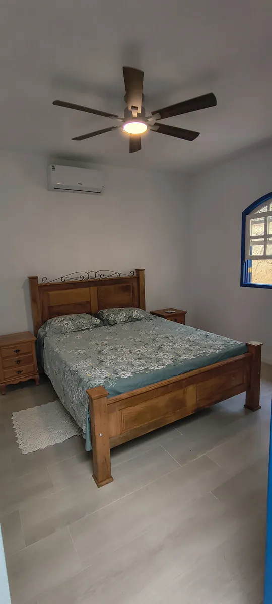 Suíte principal com cama de casal em madeira maciça, ar-condicionado e ventilador no Sítio Canto da Seriema