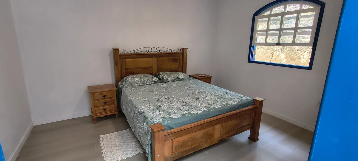 Quarto de casal com cama e criados-mudos em madeira rústica e janela colonial no Sítio Canto da Seriema