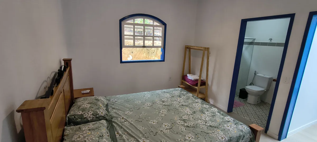 Suíte com cama de casal, arara de roupas e banheiro privativo no Sítio Canto da Seriema