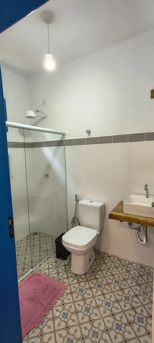 Banheiro com box de vidro, pia em madeira e piso de ladrilho artesanal no Sítio Canto da Seriema