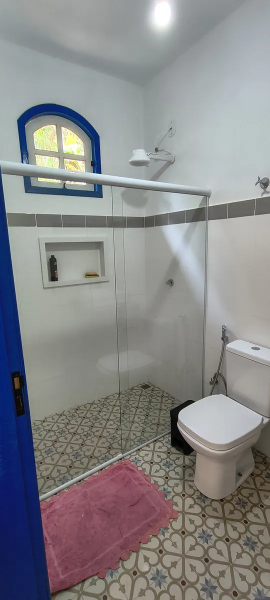 Banheiro com box de vidro, nicho para produtos e janela colonial azul no Sítio Canto da Seriema