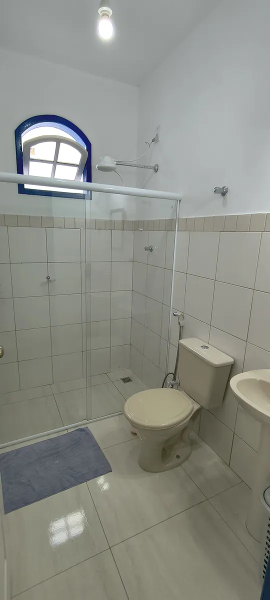 Banheiro social com box de vidro, chuveiro e janela colonial azul no Sítio Canto da Seriema