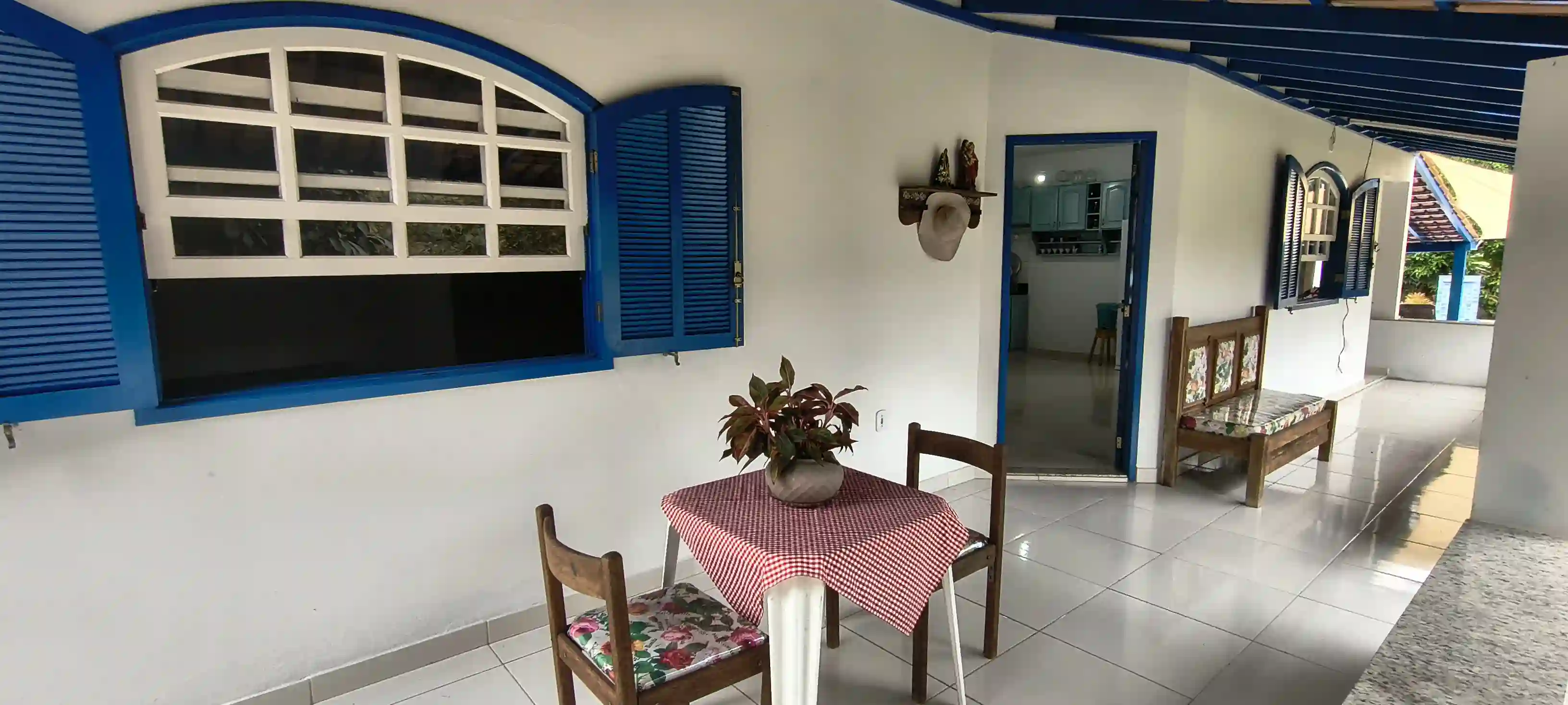 Mesa decorada com toalha xadrez vermelha e branca na varanda colonial do casarão sob a luz do dia